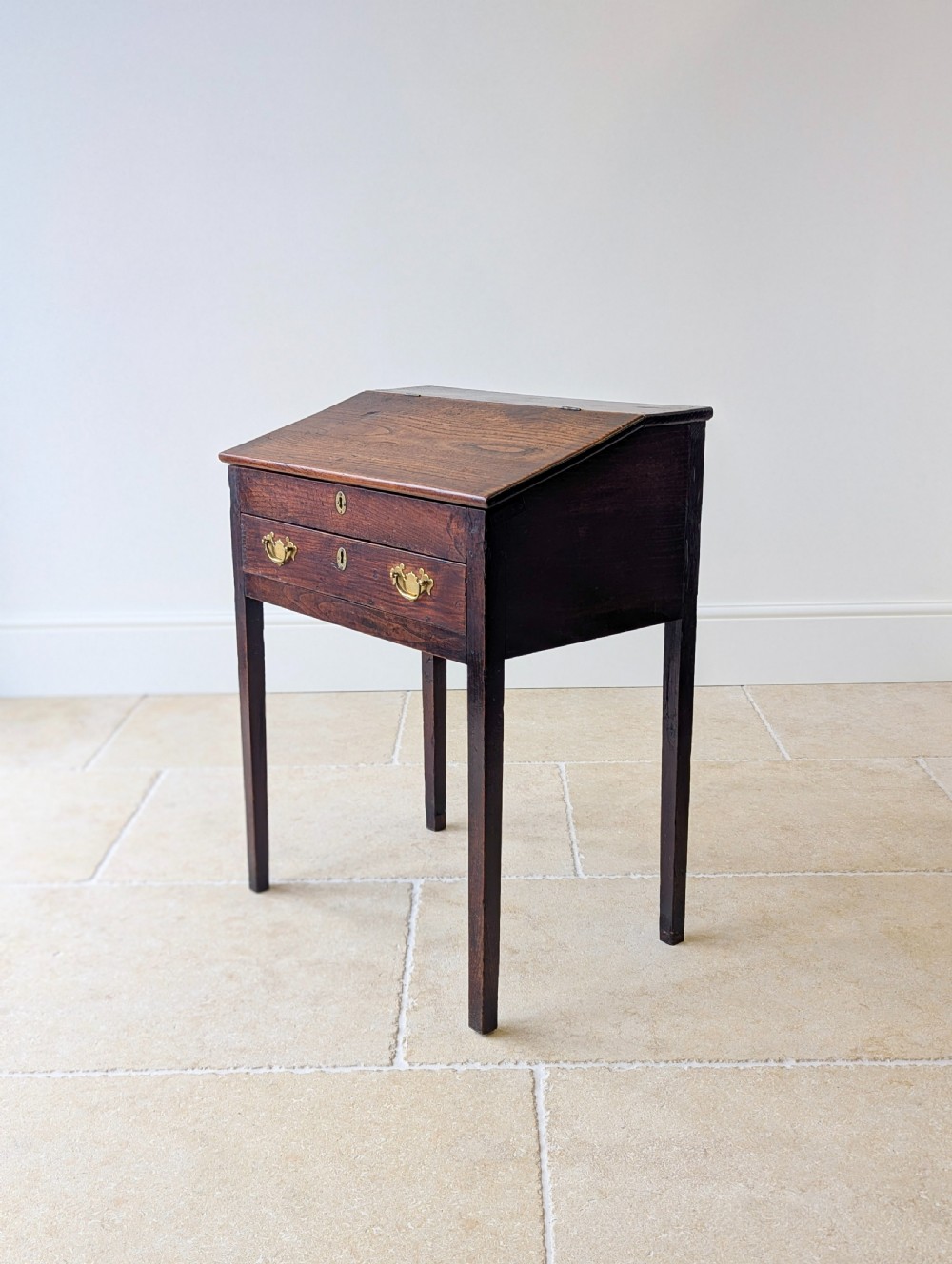 A Georgian dark elm clerks desk featuring a sloped writing surface, brass escutcheons, brass handles, and square legs. View XIII