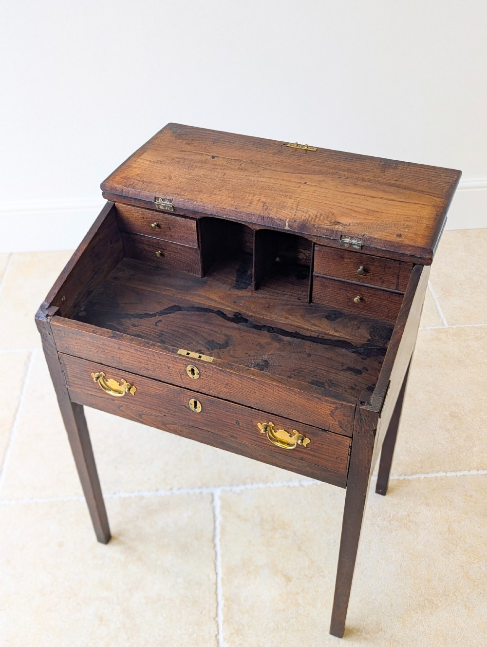 A Georgian dark elm clerks desk featuring a sloped writing surface, brass escutcheons, brass handles, and square legs. View XIV