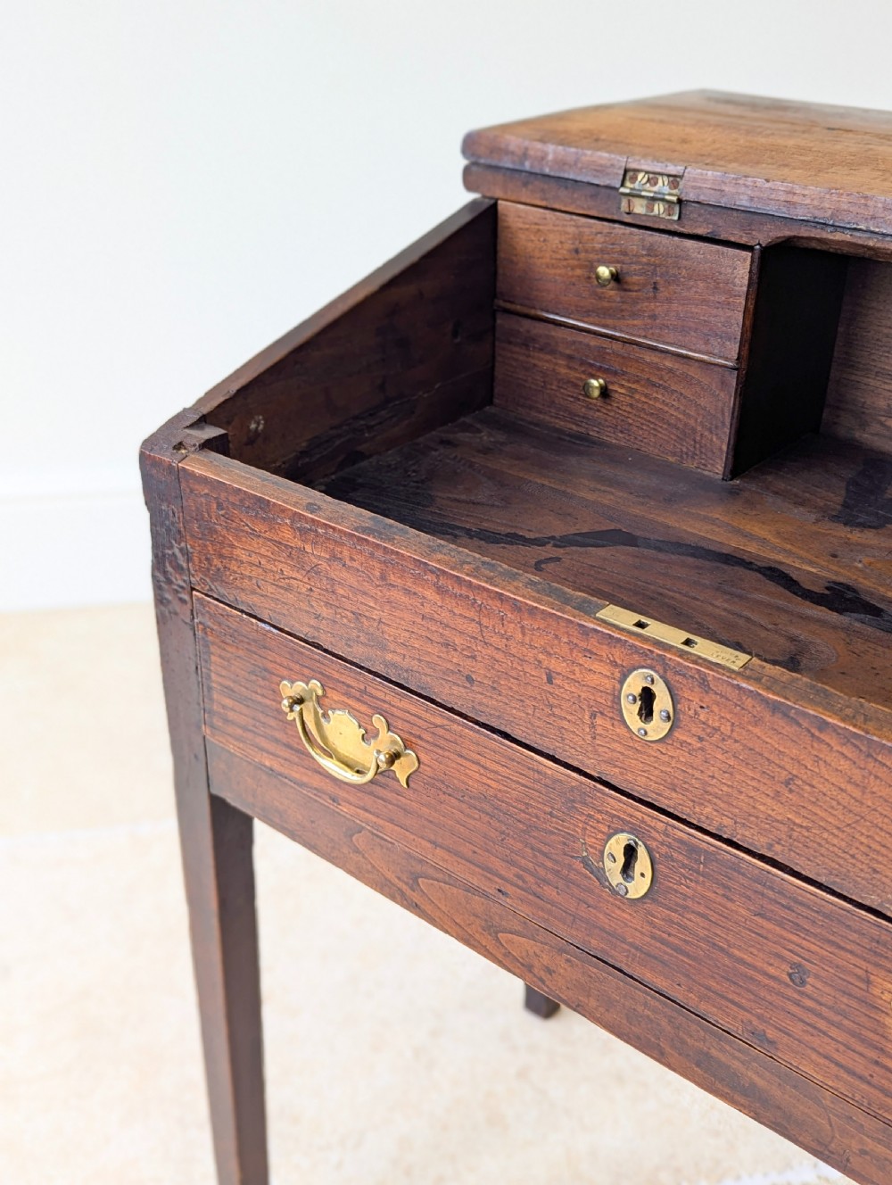 A Georgian dark elm clerks desk featuring a sloped writing surface, brass escutcheons, brass handles, and square legs. View XVI