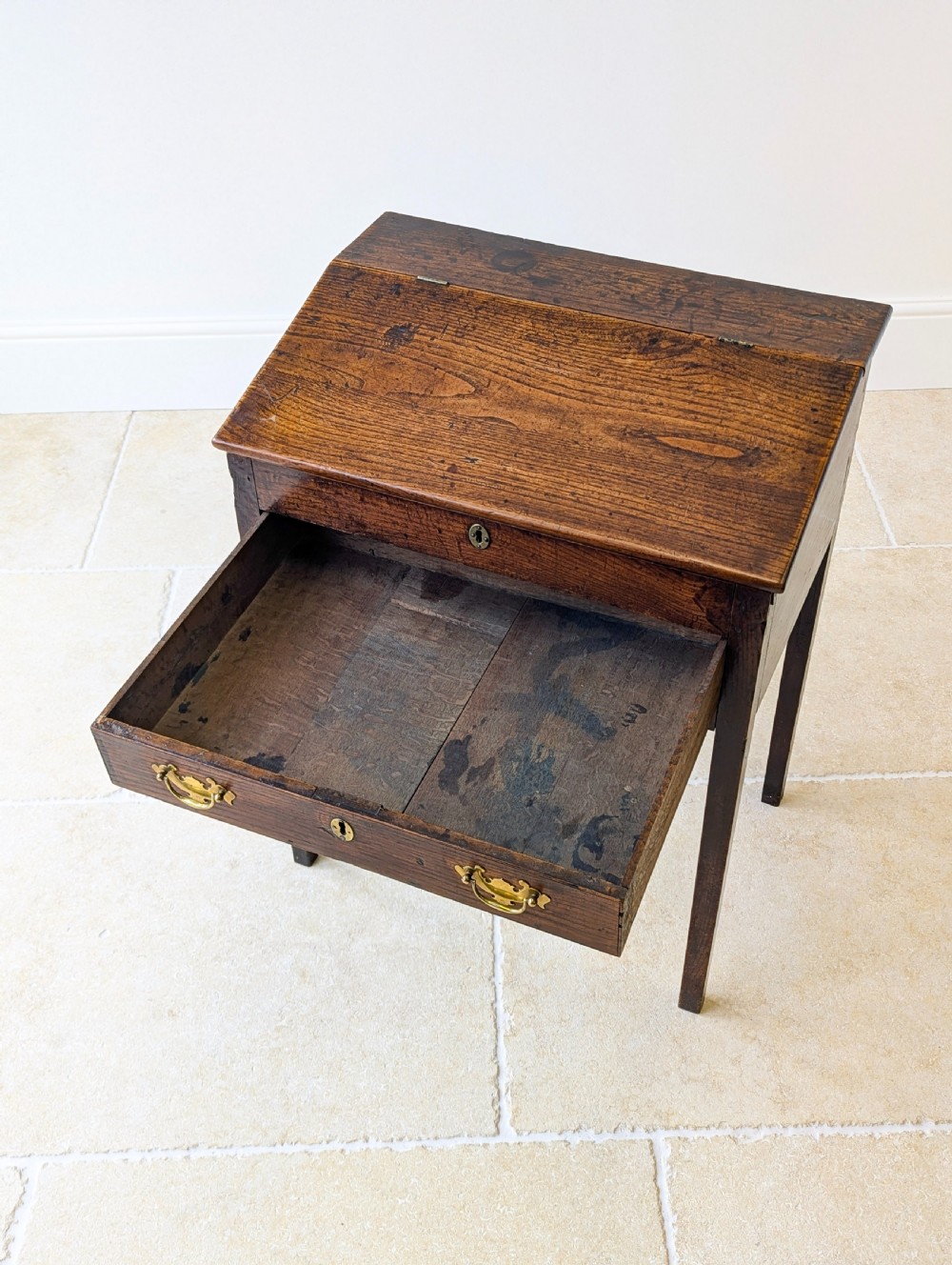 A Georgian dark elm clerks desk featuring a sloped writing surface, brass escutcheons, brass handles, and square legs. View XVII