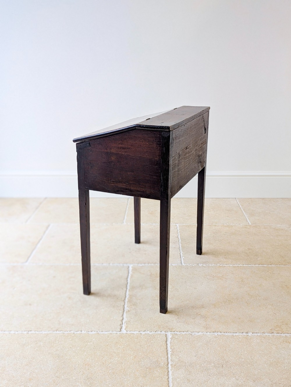 A Georgian dark elm clerks desk featuring a sloped writing surface, brass escutcheons, brass handles, and square legs. View XIX