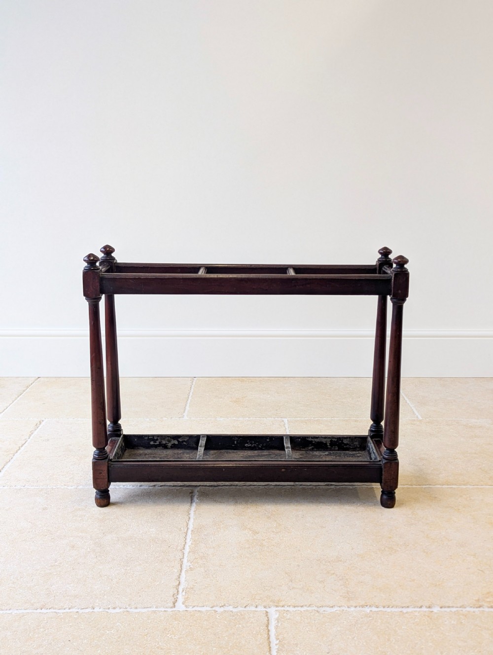 A Victorian dark mahogany stick stand featuring four turned corner supports, a partitioned upper frame, and a metal drip tray base.