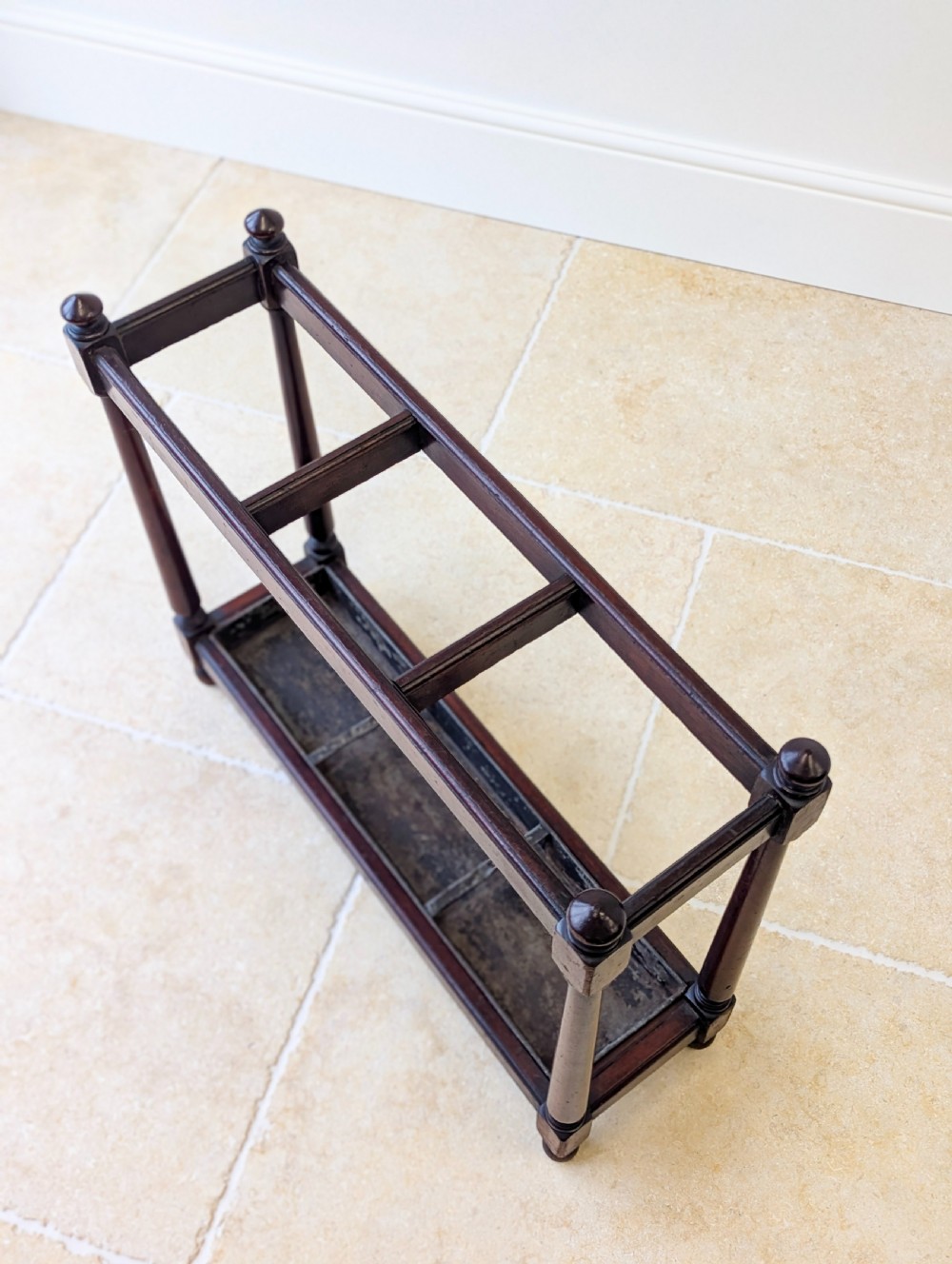 A Victorian dark mahogany stick stand featuring four turned corner supports, a partitioned upper frame, and a metal drip tray base. View VII