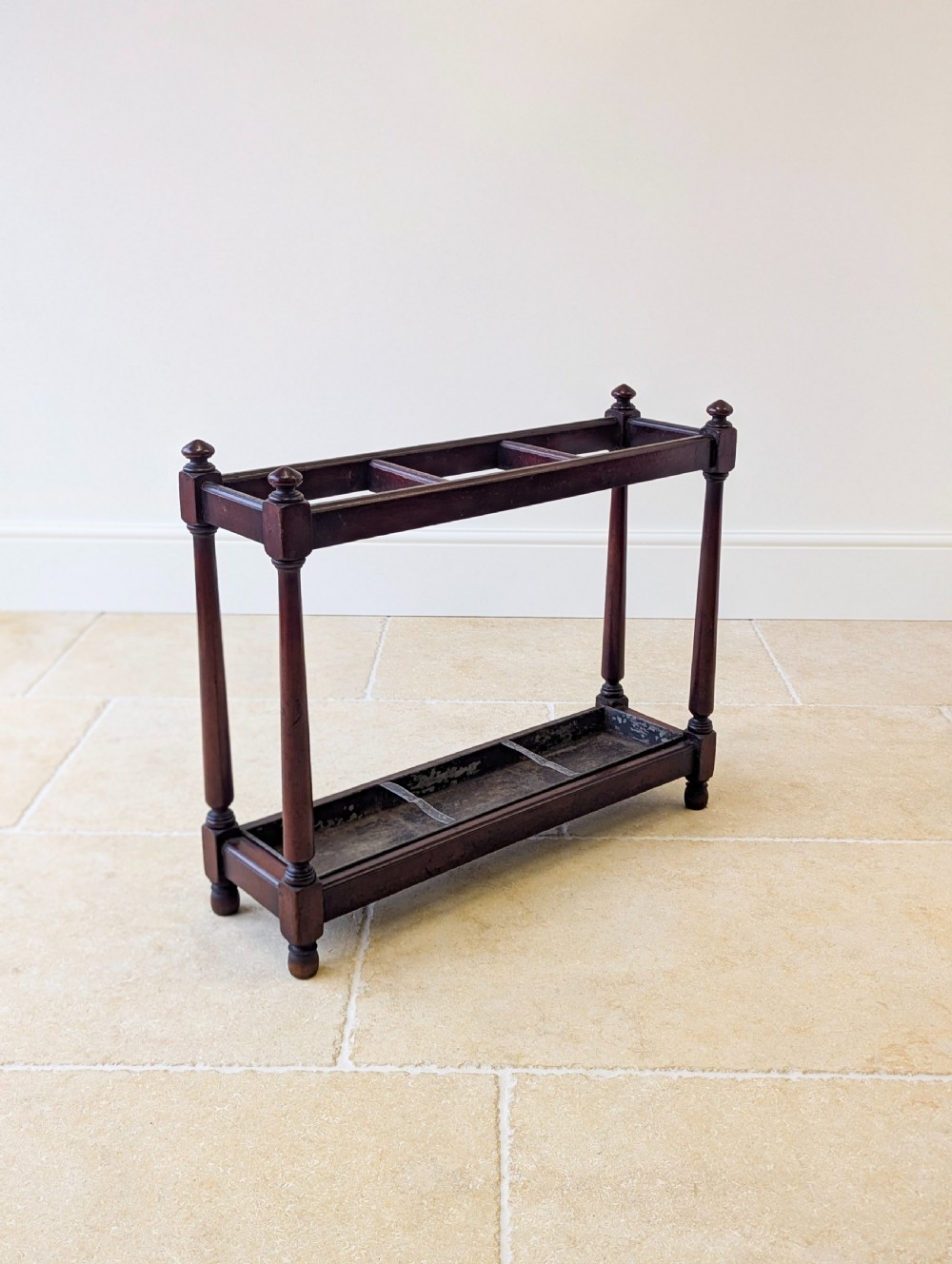 A Victorian dark mahogany stick stand featuring four turned corner supports, a partitioned upper frame, and a metal drip tray base. View X