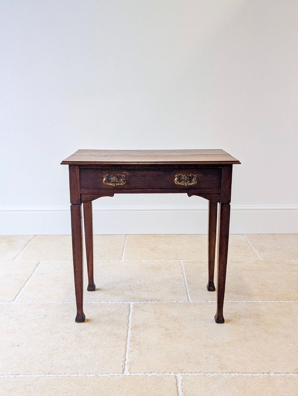 An antique dark oak side table featuring a single drawer with brass drop handles, shaped corner aprons, and slender tapered legs. View III