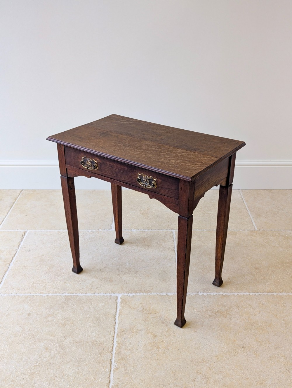 An antique dark oak side table featuring a single drawer with brass drop handles, shaped corner aprons, and slender tapered legs. View V