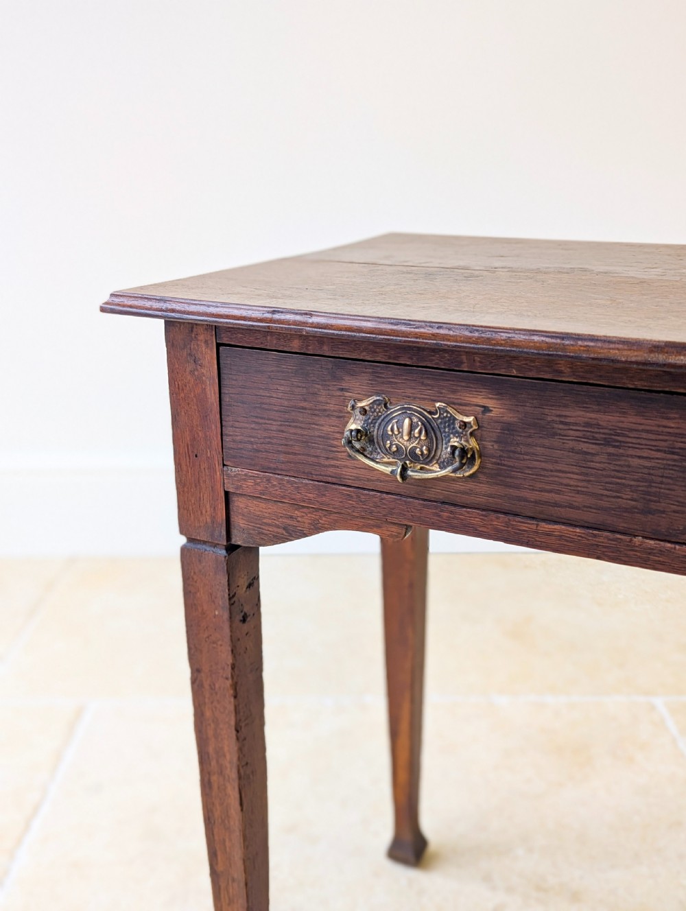 An antique dark oak side table featuring a single drawer with brass drop handles, shaped corner aprons, and slender tapered legs. View VI