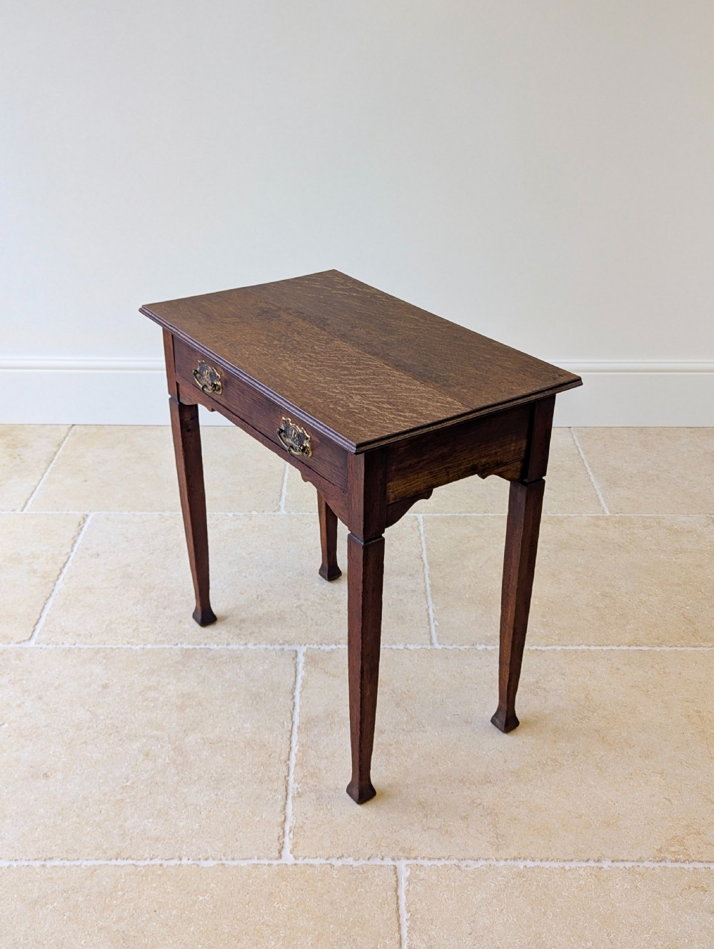 An antique dark oak side table featuring a single drawer with brass drop handles, shaped corner aprons, and slender tapered legs. View VII