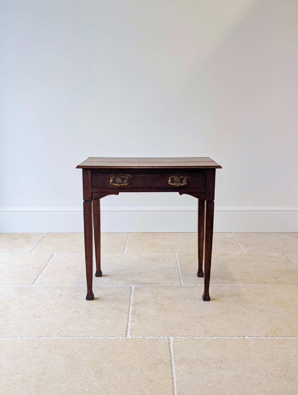 An antique dark oak side table featuring a single drawer with brass drop handles, shaped corner aprons, and slender tapered legs. View VIII