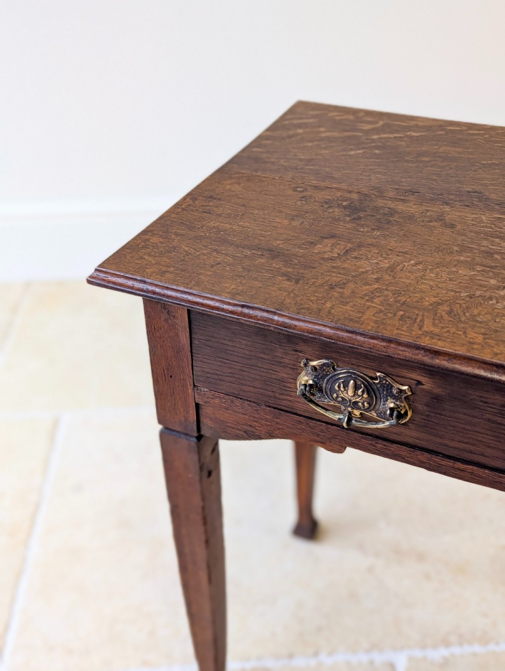 An antique dark oak side table featuring a single drawer with brass drop handles, shaped corner aprons, and slender tapered legs. View IX