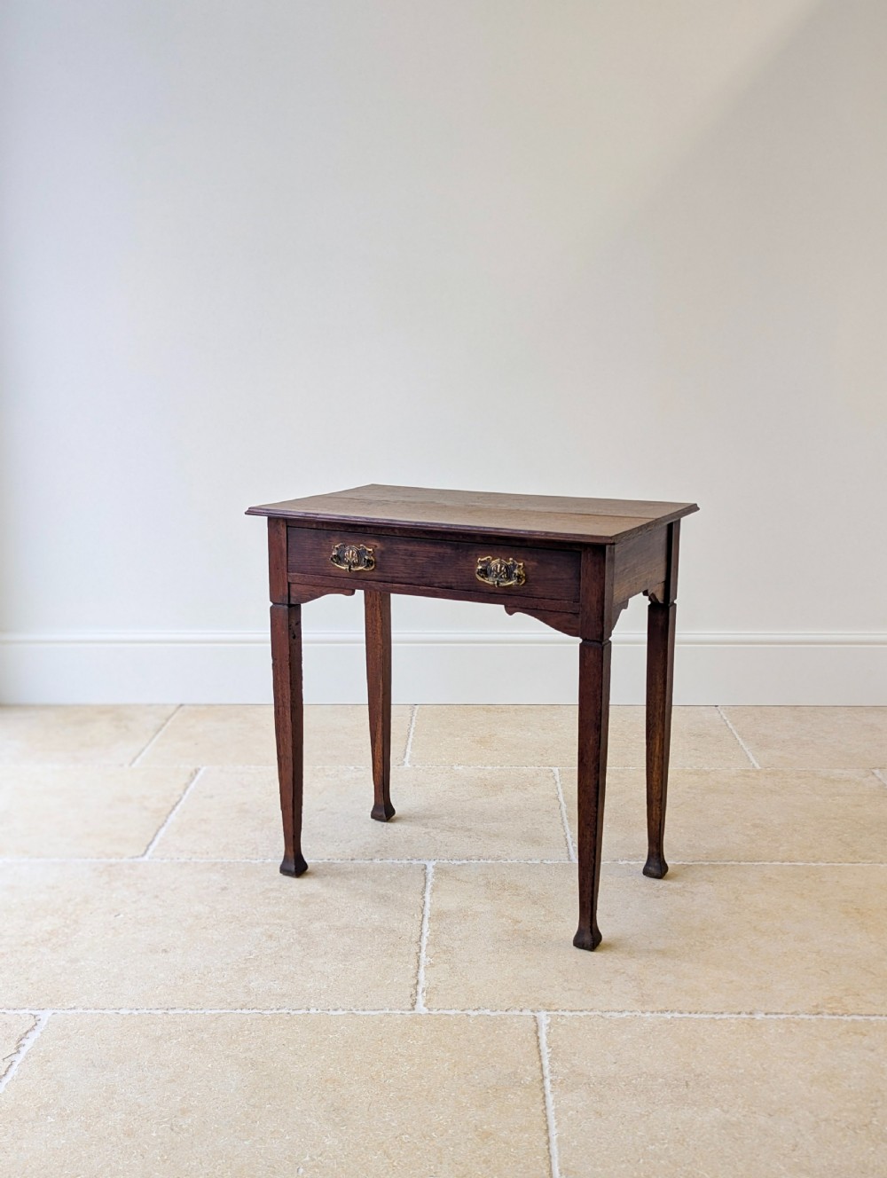 An antique dark oak side table featuring a single drawer with brass drop handles, shaped corner aprons, and slender tapered legs. View XII