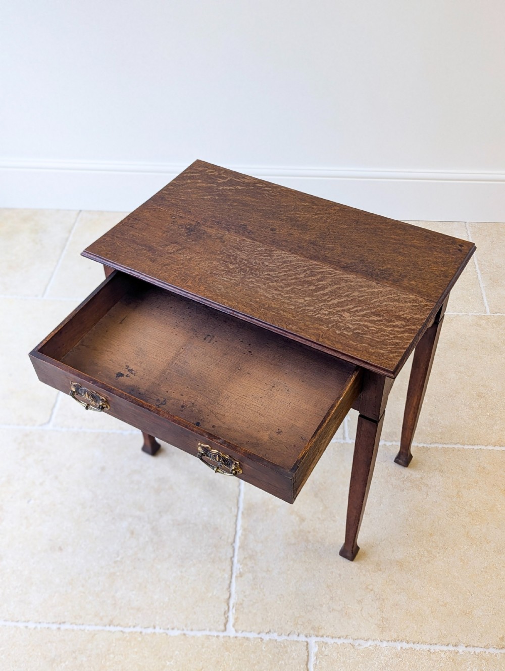 An antique dark oak side table featuring a single drawer with brass drop handles, shaped corner aprons, and slender tapered legs. View XIII