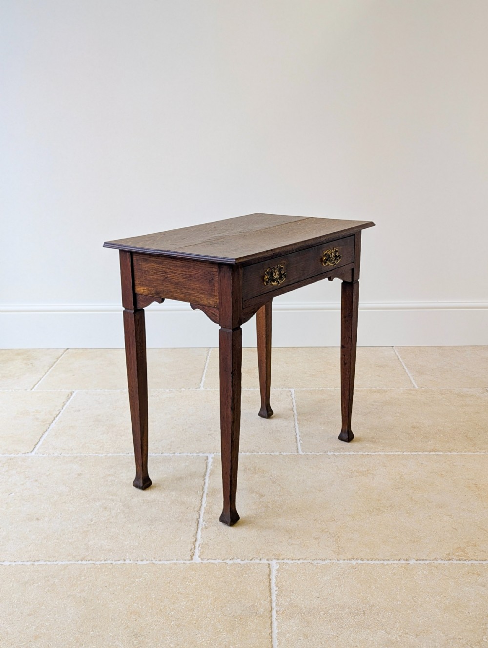 An antique dark oak side table featuring a single drawer with brass drop handles, shaped corner aprons, and slender tapered legs. View XIV