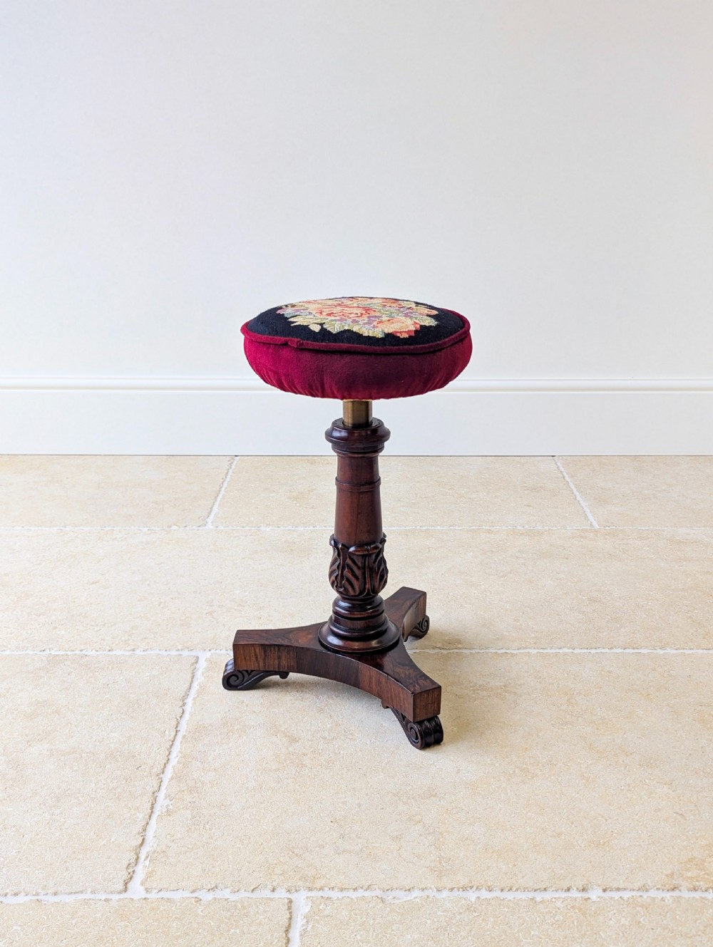A William IV rosewood adjustable piano stool featuring a circular floral needlepoint seat with burgundy velvet trim, supported by a carved pedestal and triform base. View V