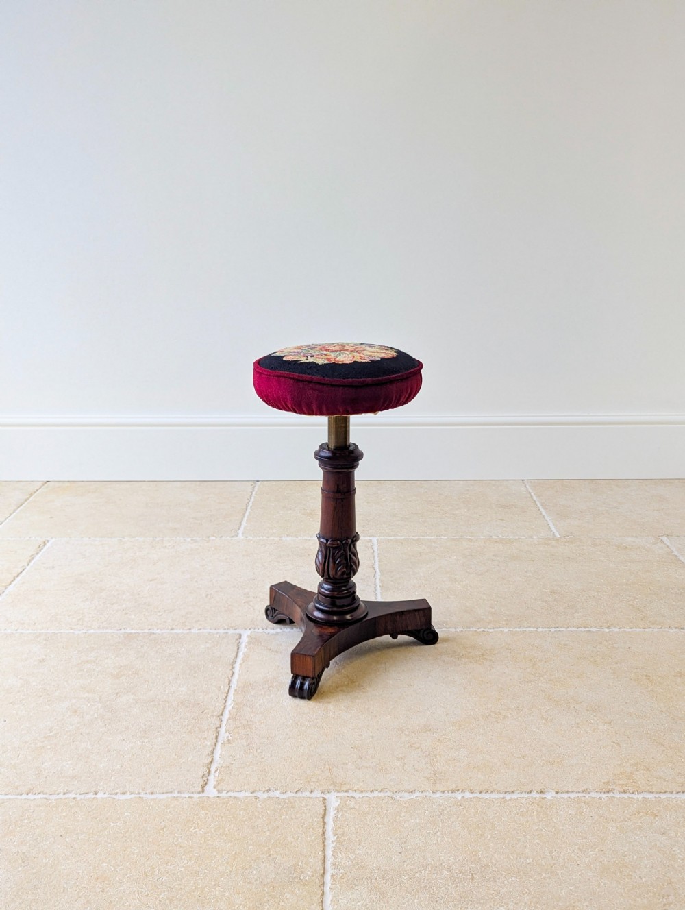 A William IV rosewood adjustable piano stool featuring a circular floral needlepoint seat with burgundy velvet trim, supported by a carved pedestal and triform base. View VII