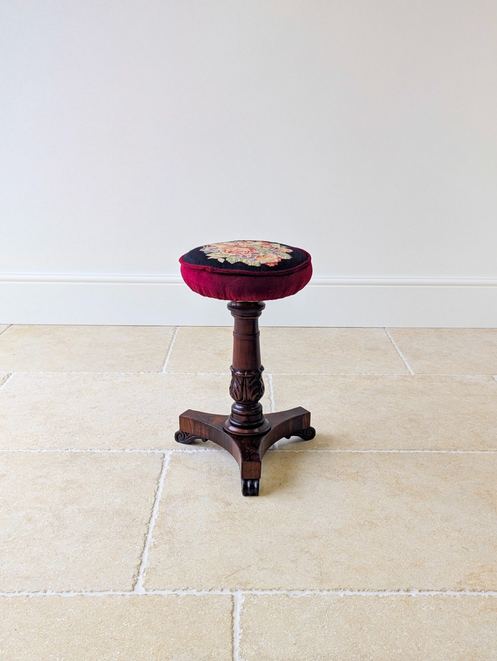 A William IV rosewood adjustable piano stool featuring a circular floral needlepoint seat with burgundy velvet trim, supported by a carved pedestal and triform base. View IX