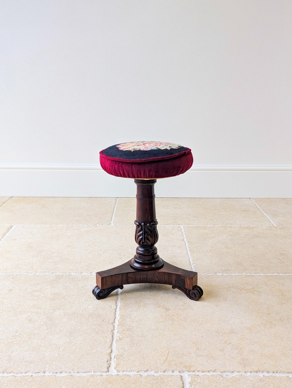 A William IV rosewood adjustable piano stool featuring a circular floral needlepoint seat with burgundy velvet trim, supported by a carved pedestal and triform base. View XI