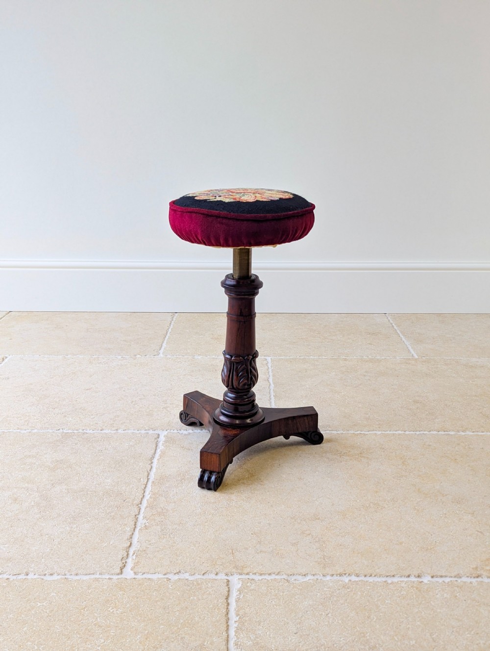 A William IV rosewood adjustable piano stool featuring a circular floral needlepoint seat with burgundy velvet trim, supported by a carved pedestal and triform base. View XVII
