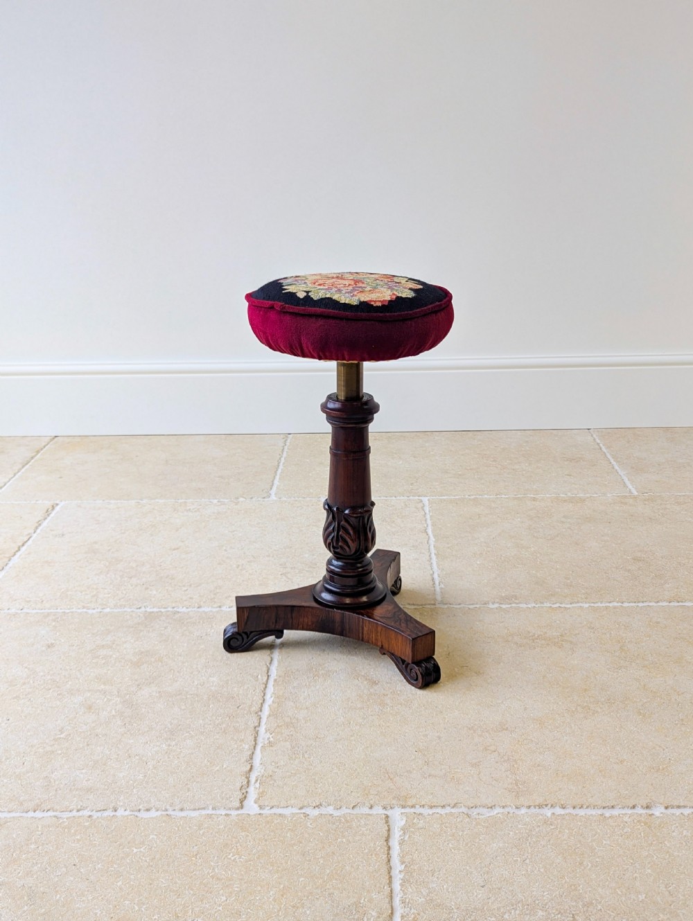 A William IV rosewood adjustable piano stool featuring a circular floral needlepoint seat with burgundy velvet trim, supported by a carved pedestal and triform base. View XIX