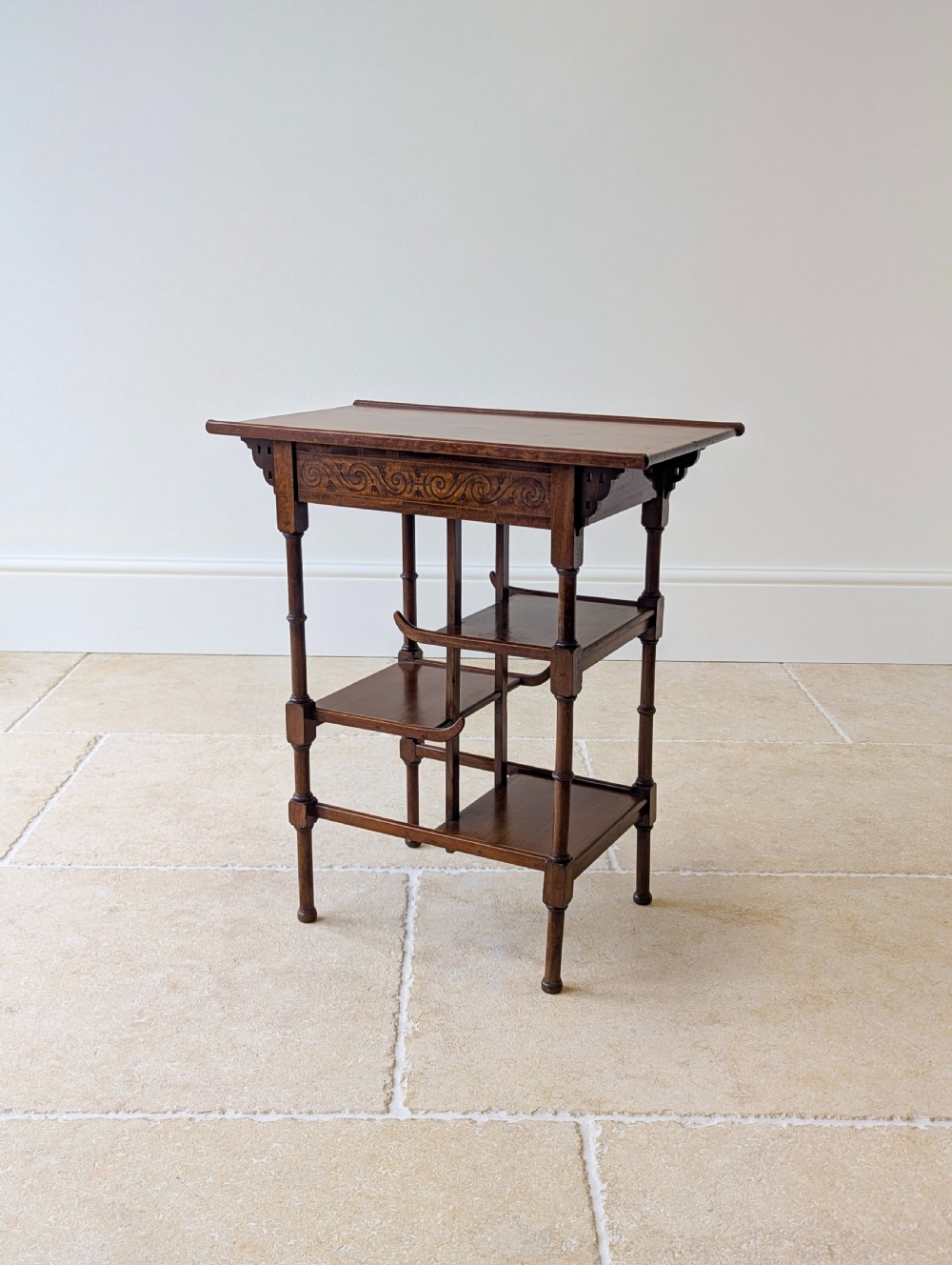 An Edwardian mahogany Anglo-Japanese occasional table with a pagoda-style top, carved scroll apron, and tiered display shelves on turned legs.