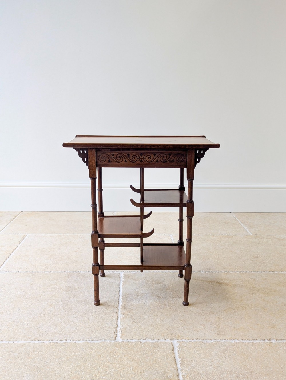 An Edwardian mahogany Anglo-Japanese occasional table with a pagoda-style top, carved scroll apron, and tiered display shelves on turned legs. View II