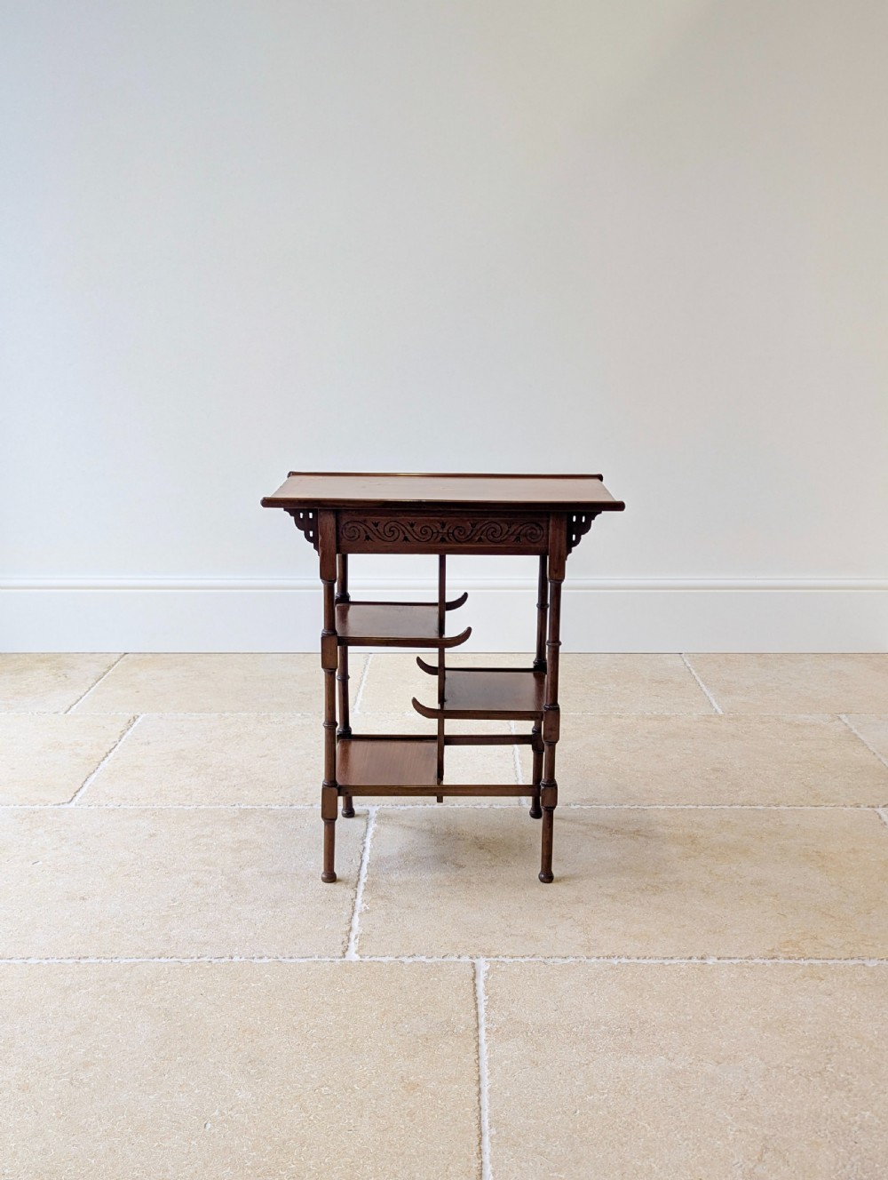 An Edwardian mahogany Anglo-Japanese occasional table with a pagoda-style top, carved scroll apron, and tiered display shelves on turned legs. View V