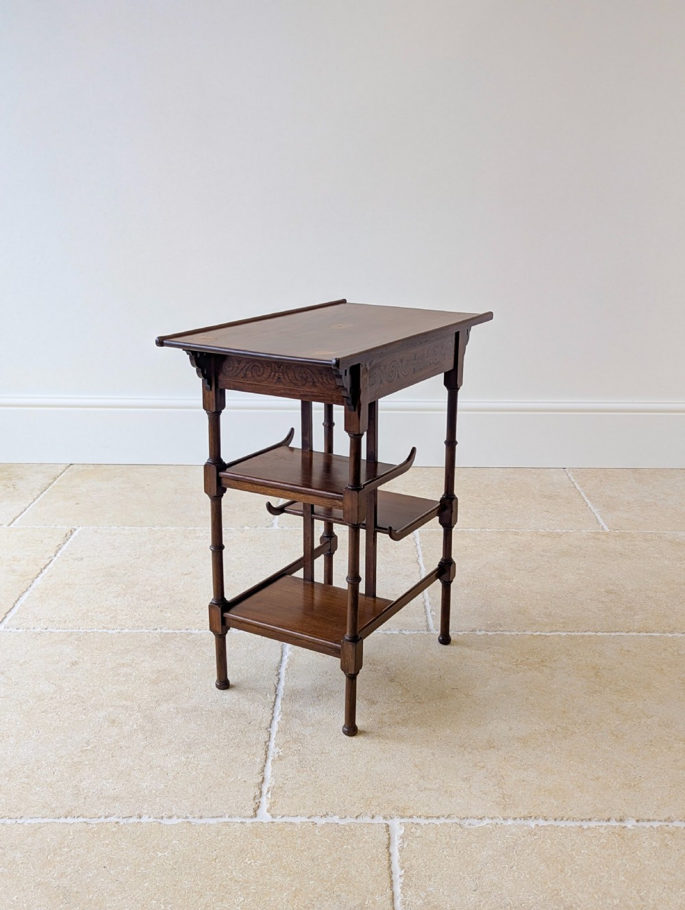 An Edwardian mahogany Anglo-Japanese occasional table with a pagoda-style top, carved scroll apron, and tiered display shelves on turned legs. View VII