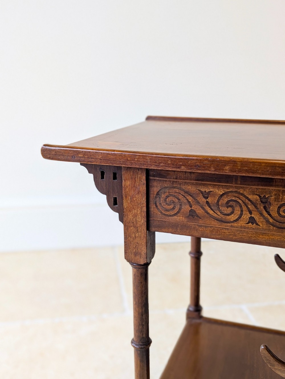 An Edwardian mahogany Anglo-Japanese occasional table with a pagoda-style top, carved scroll apron, and tiered display shelves on turned legs. View VIII