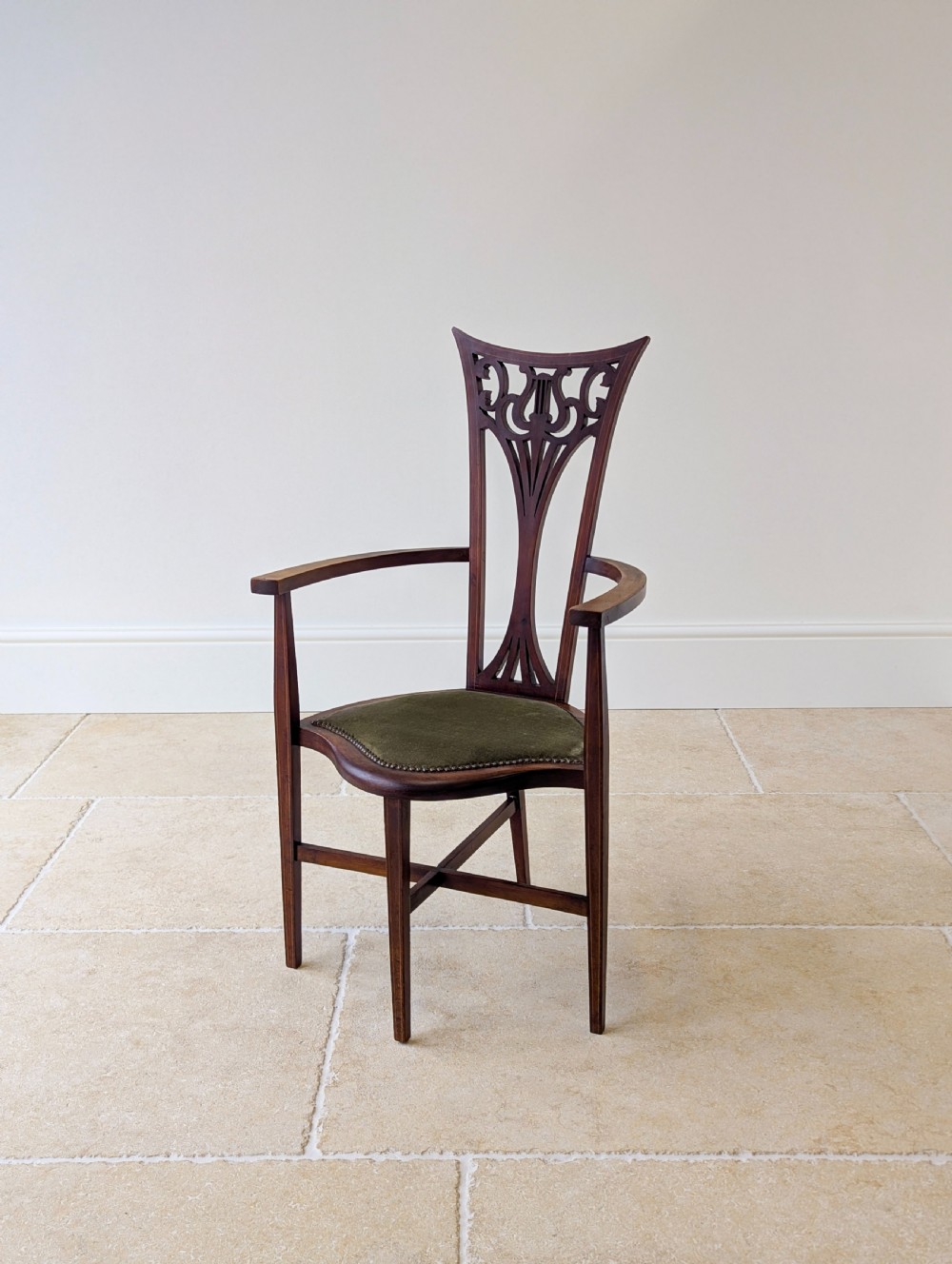 An Edwardian mahogany elbow chair featuring a high pierced back splat, swept arms, and an olive green velvet upholstered seat.