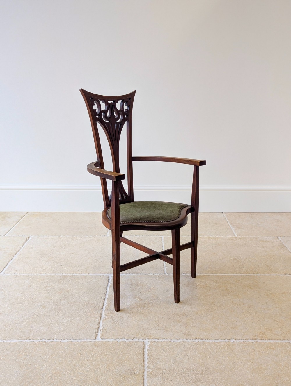 An Edwardian mahogany elbow chair featuring a high pierced back splat, swept arms, and an olive green velvet upholstered seat. View V