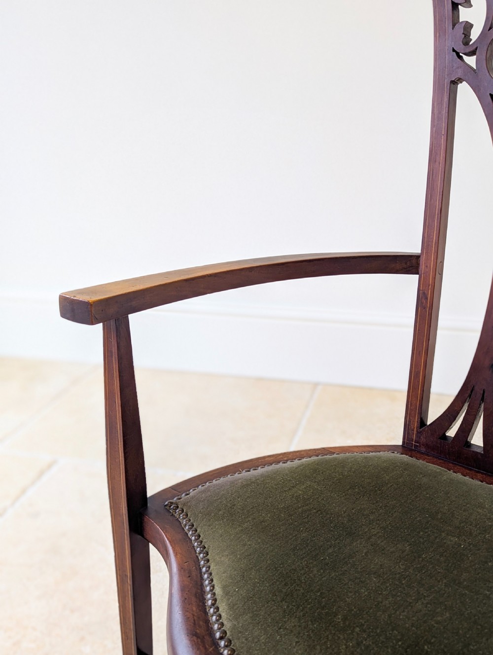 An Edwardian mahogany elbow chair featuring a high pierced back splat, swept arms, and an olive green velvet upholstered seat. View VI