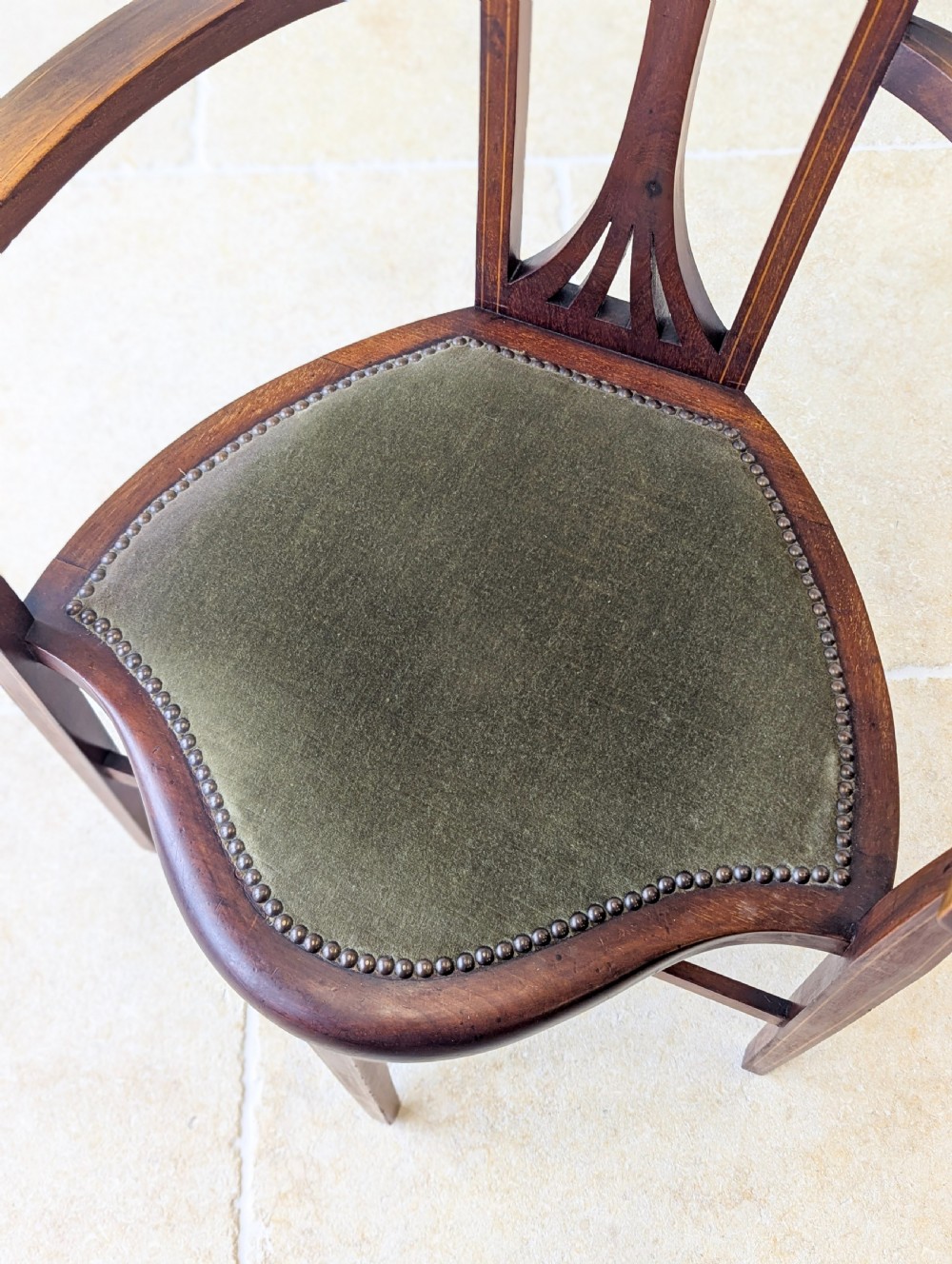 An Edwardian mahogany elbow chair featuring a high pierced back splat, swept arms, and an olive green velvet upholstered seat. View VII