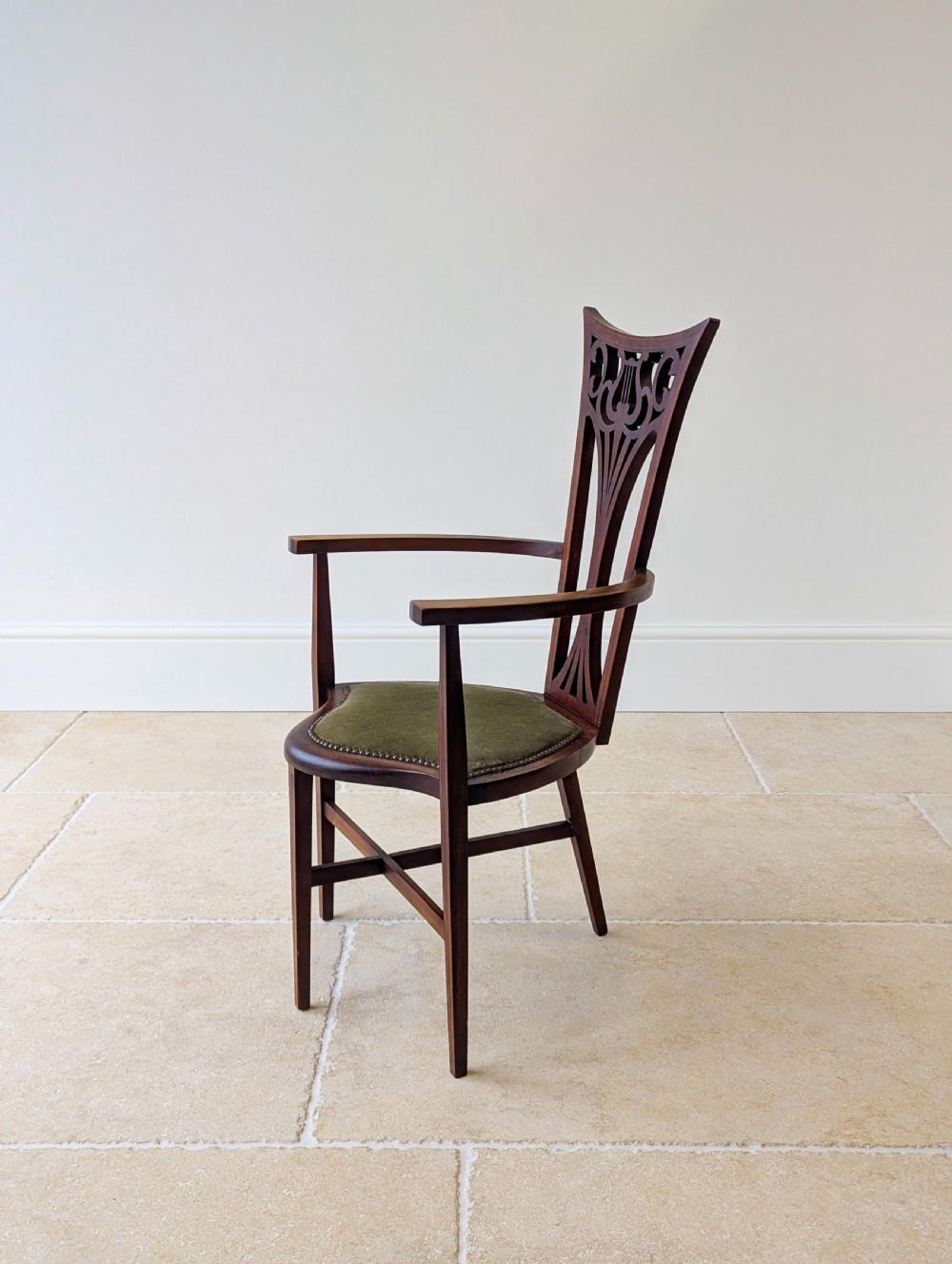An Edwardian mahogany elbow chair featuring a high pierced back splat, swept arms, and an olive green velvet upholstered seat. View X
