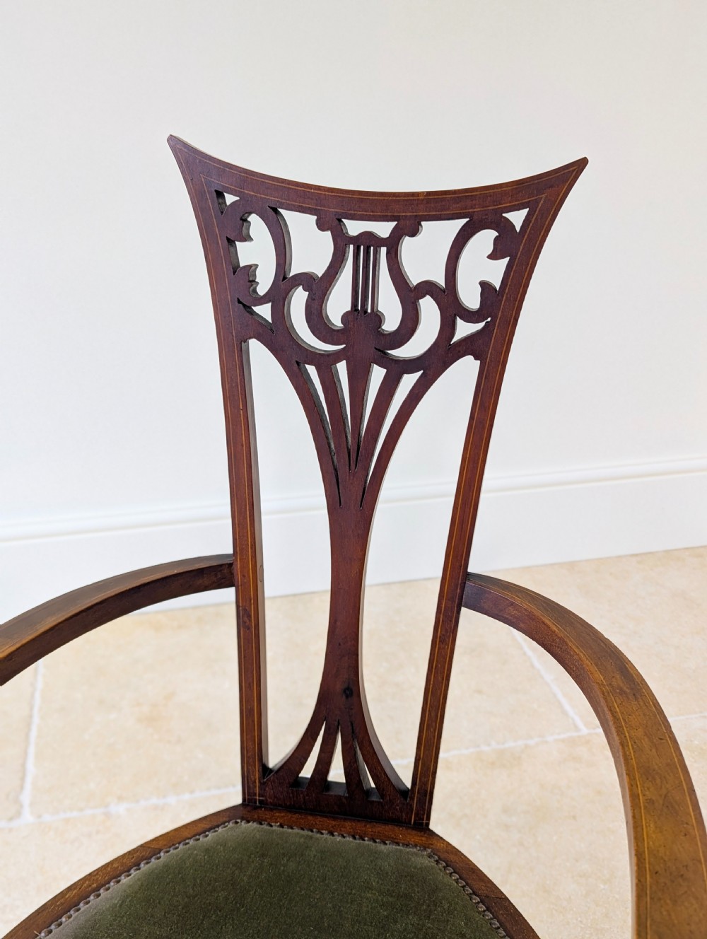 An Edwardian mahogany elbow chair featuring a high pierced back splat, swept arms, and an olive green velvet upholstered seat. View XV
