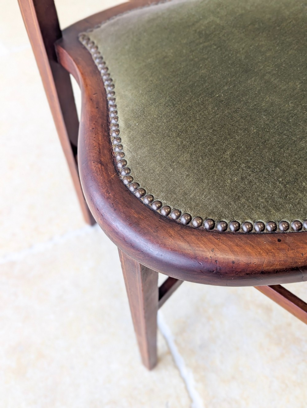 An Edwardian mahogany elbow chair featuring a high pierced back splat, swept arms, and an olive green velvet upholstered seat. View XVI