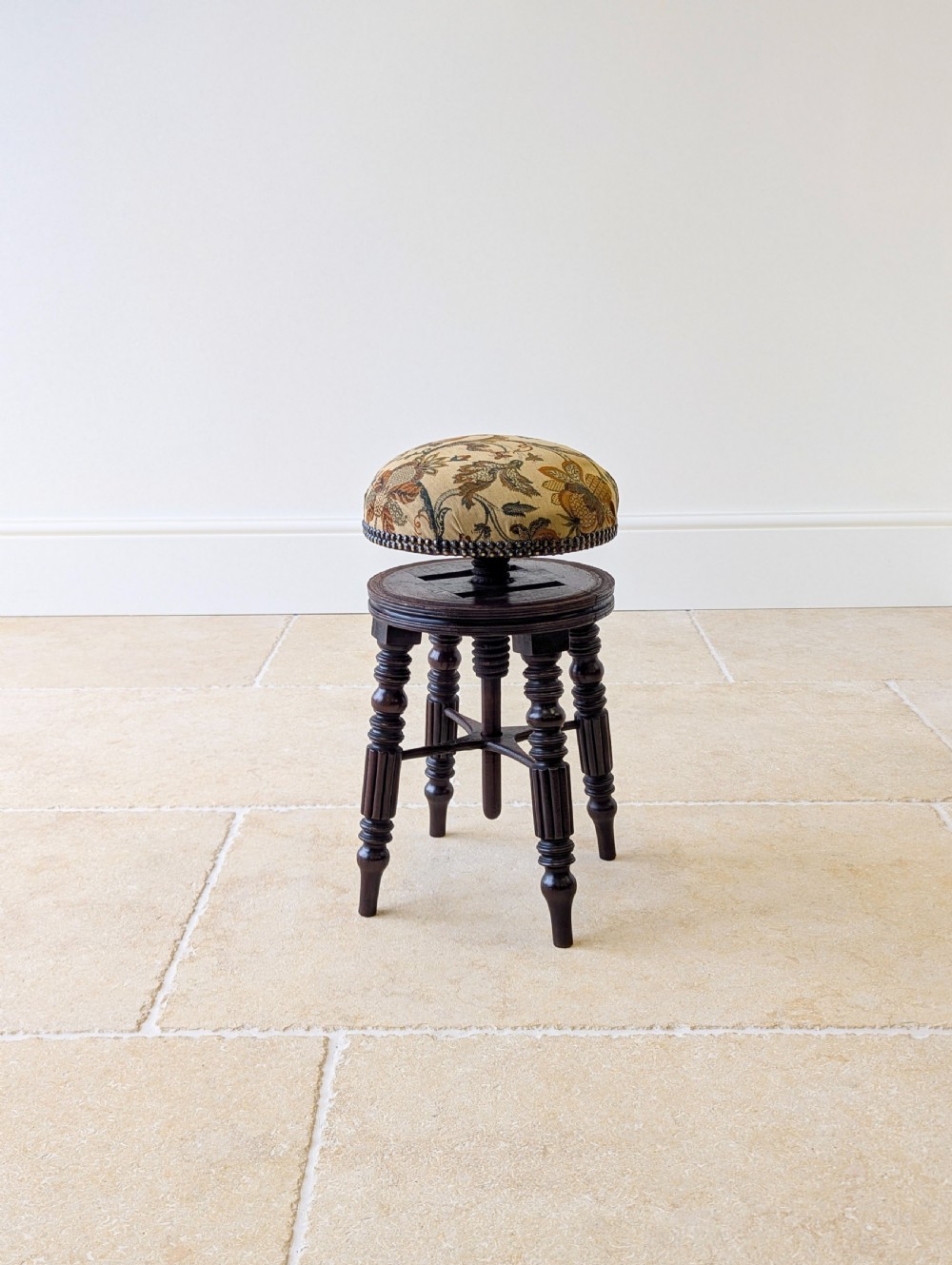 A Victorian dark mahogany adjustable piano stool featuring four turned legs, a threaded centre spindle, and a circular patterned fabric seat trimmed with brass studs.