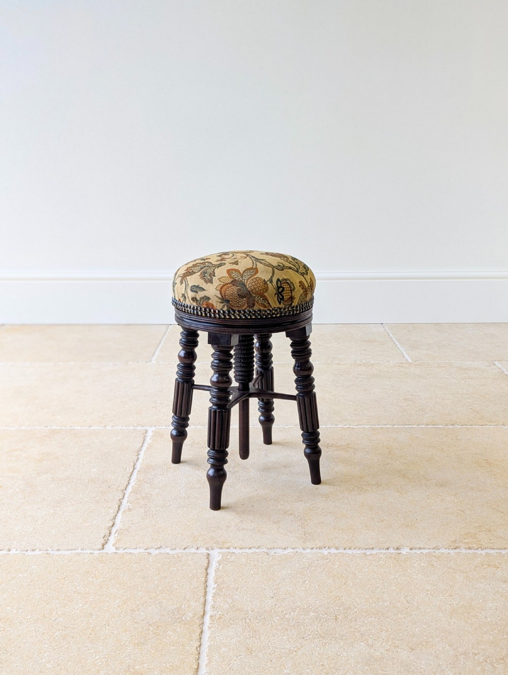 A Victorian dark mahogany adjustable piano stool featuring four turned legs, a threaded centre spindle, and a circular patterned fabric seat trimmed with brass studs. View II