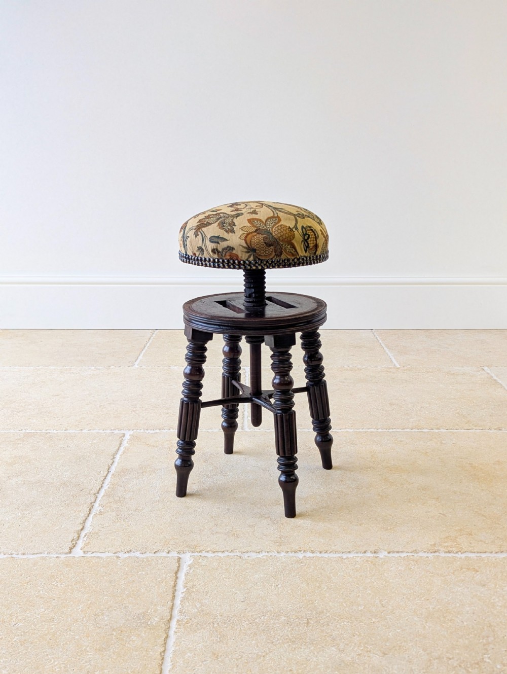 A Victorian dark mahogany adjustable piano stool featuring four turned legs, a threaded centre spindle, and a circular patterned fabric seat trimmed with brass studs. View III