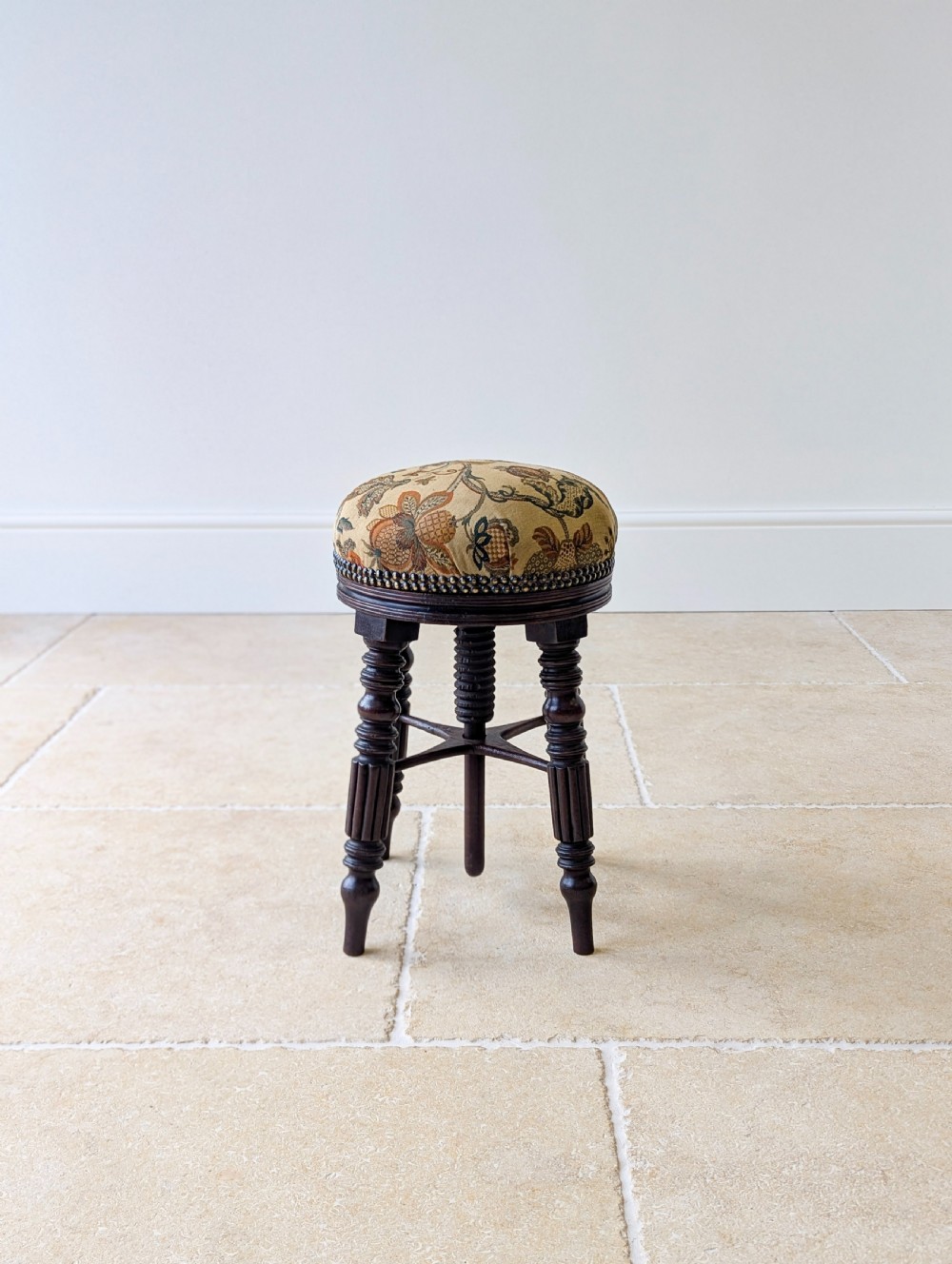A Victorian dark mahogany adjustable piano stool featuring four turned legs, a threaded centre spindle, and a circular patterned fabric seat trimmed with brass studs. View V