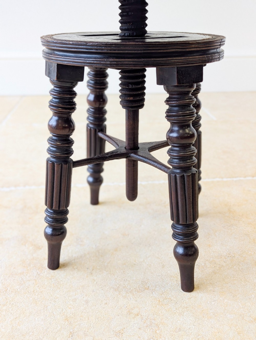 A Victorian dark mahogany adjustable piano stool featuring four turned legs, a threaded centre spindle, and a circular patterned fabric seat trimmed with brass studs. View VIII