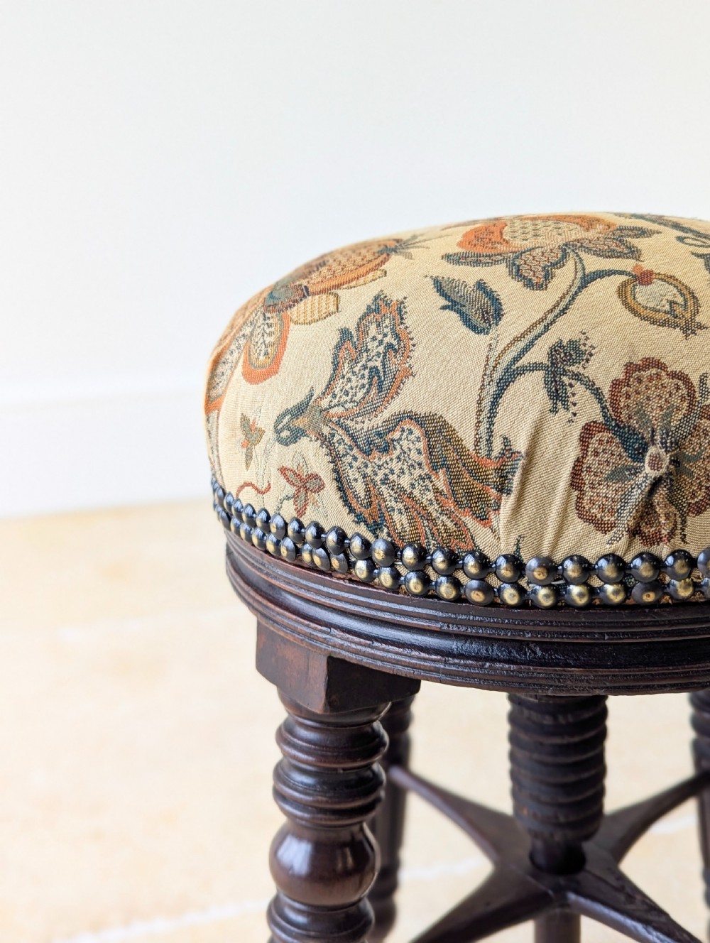 A Victorian dark mahogany adjustable piano stool featuring four turned legs, a threaded centre spindle, and a circular patterned fabric seat trimmed with brass studs. View XI