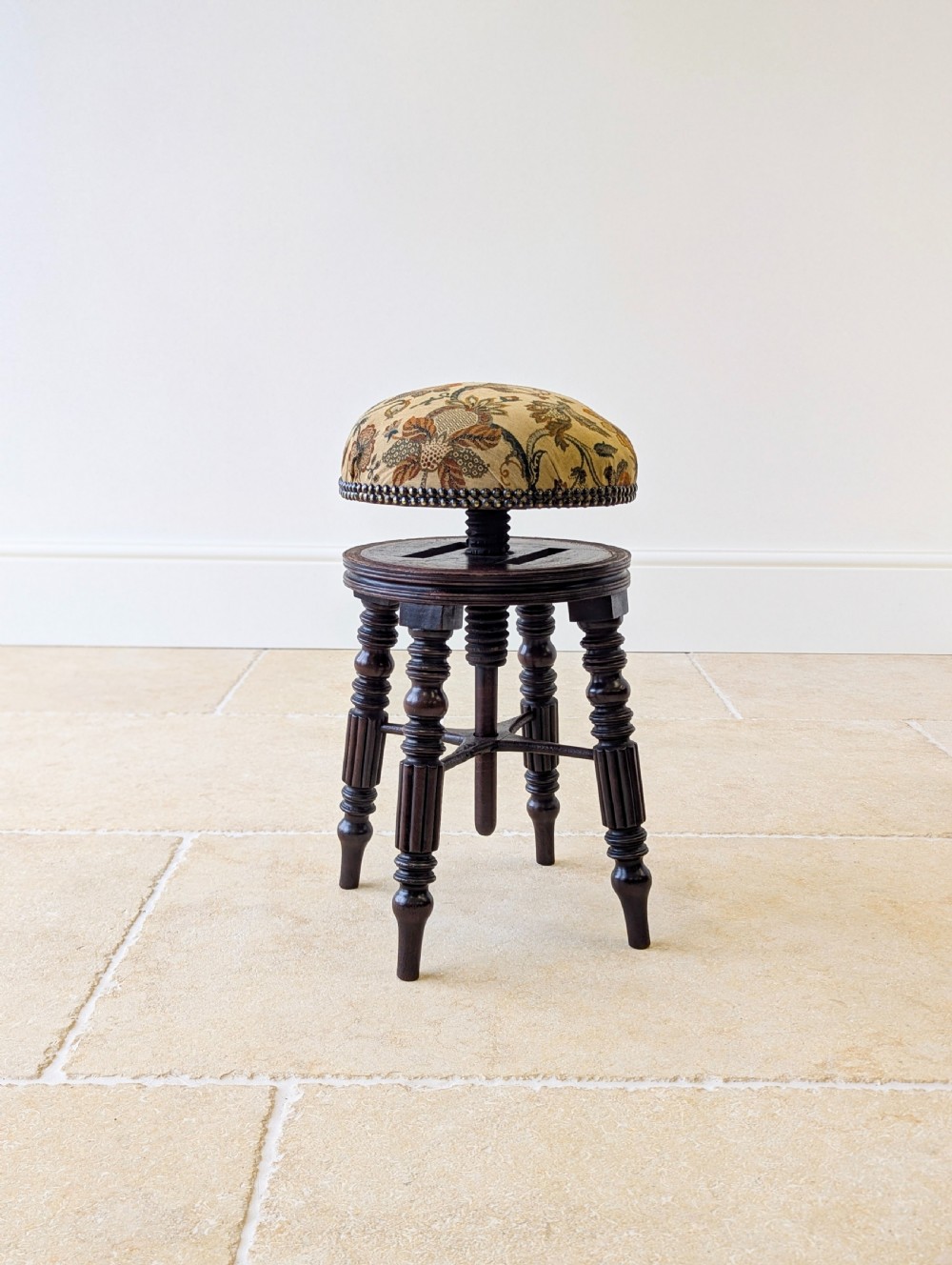 A Victorian dark mahogany adjustable piano stool featuring four turned legs, a threaded centre spindle, and a circular patterned fabric seat trimmed with brass studs. View XII