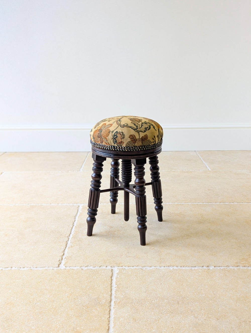 A Victorian dark mahogany adjustable piano stool featuring four turned legs, a threaded centre spindle, and a circular patterned fabric seat trimmed with brass studs. View XIII