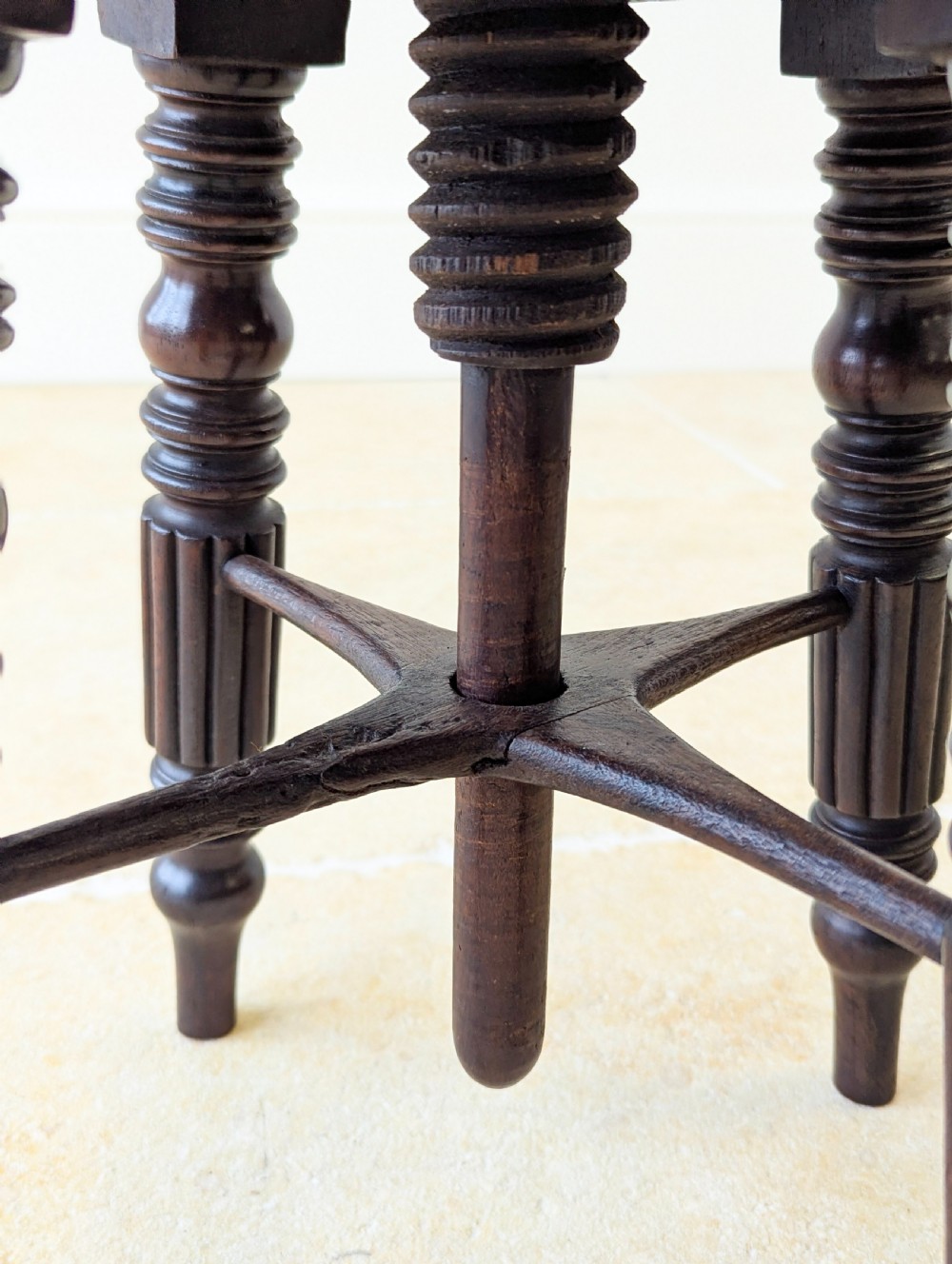 A Victorian dark mahogany adjustable piano stool featuring four turned legs, a threaded centre spindle, and a circular patterned fabric seat trimmed with brass studs. View XIV
