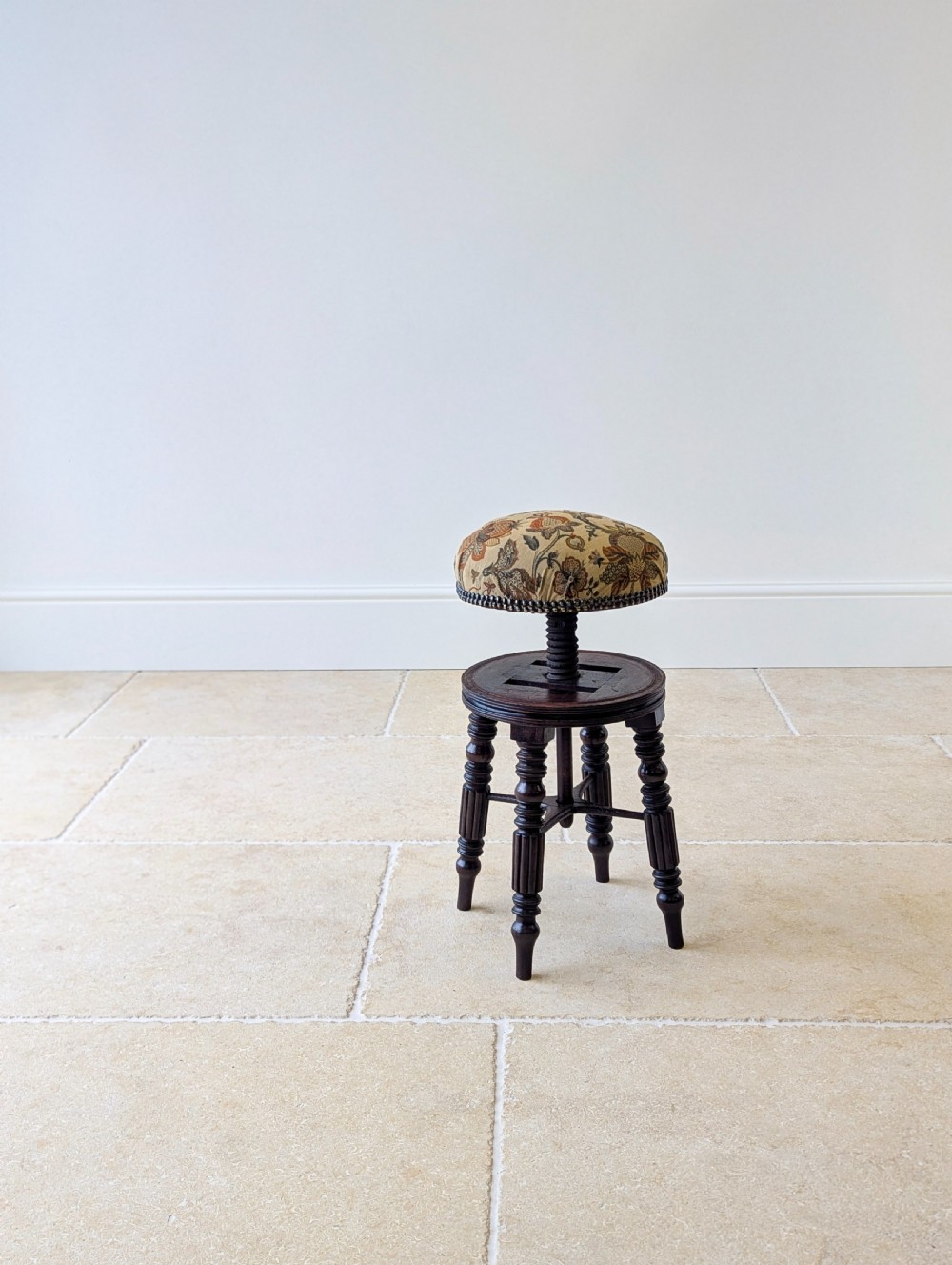 A Victorian dark mahogany adjustable piano stool featuring four turned legs, a threaded centre spindle, and a circular patterned fabric seat trimmed with brass studs. View XV