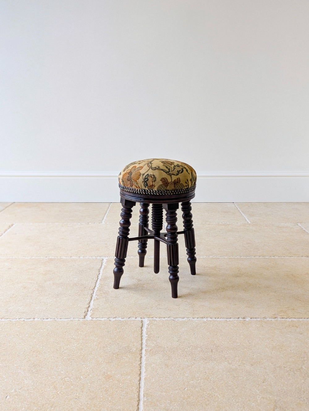 A Victorian dark mahogany adjustable piano stool featuring four turned legs, a threaded centre spindle, and a circular patterned fabric seat trimmed with brass studs. View XVI