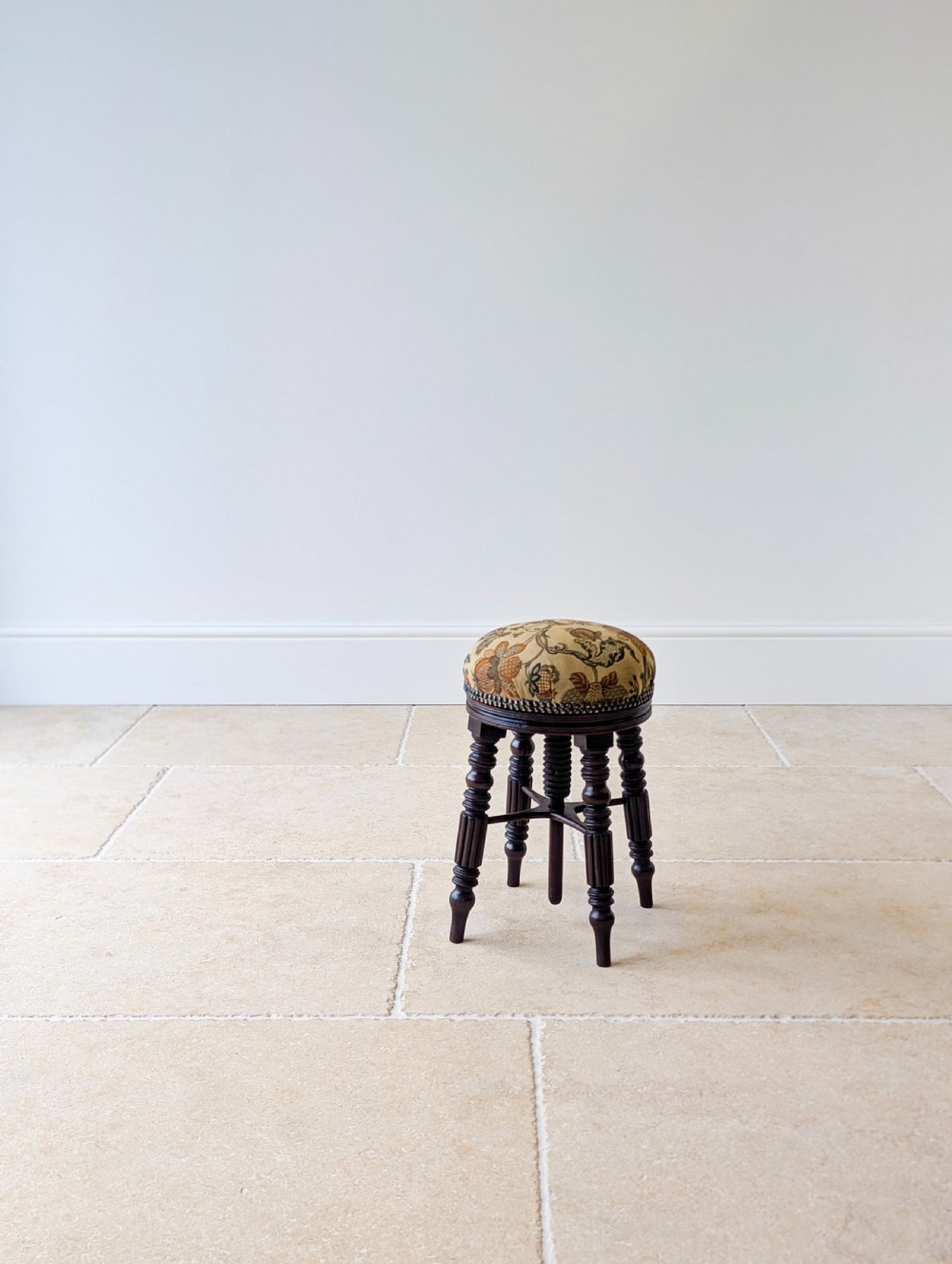 A Victorian dark mahogany adjustable piano stool featuring four turned legs, a threaded centre spindle, and a circular patterned fabric seat trimmed with brass studs. View XVIII