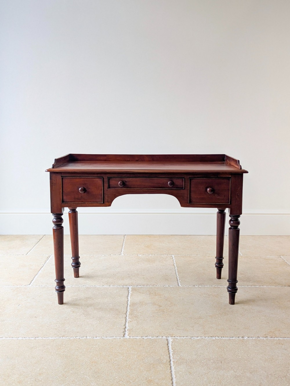 A late Victorian mahogany writing table featuring a low gallery top, three frieze drawers with turned wooden knobs, an arched kneehole, and four turned legs. View II
