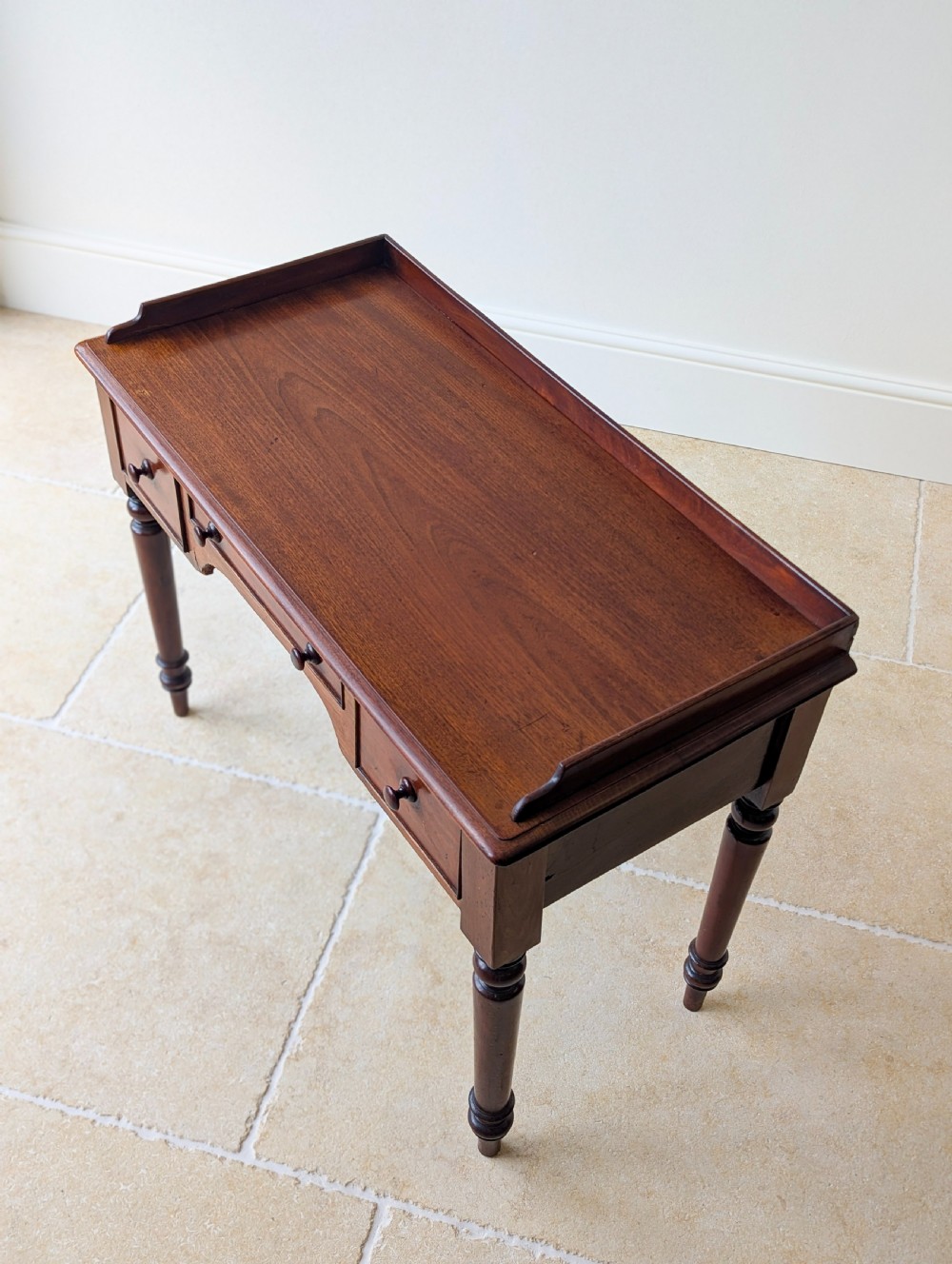 A late Victorian mahogany writing table featuring a low gallery top, three frieze drawers with turned wooden knobs, an arched kneehole, and four turned legs. View III