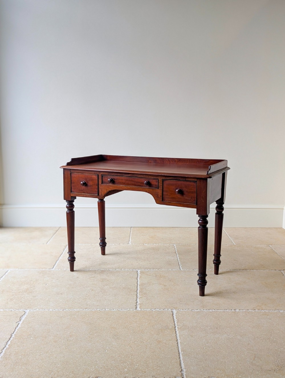 A late Victorian mahogany writing table featuring a low gallery top, three frieze drawers with turned wooden knobs, an arched kneehole, and four turned legs. View IV